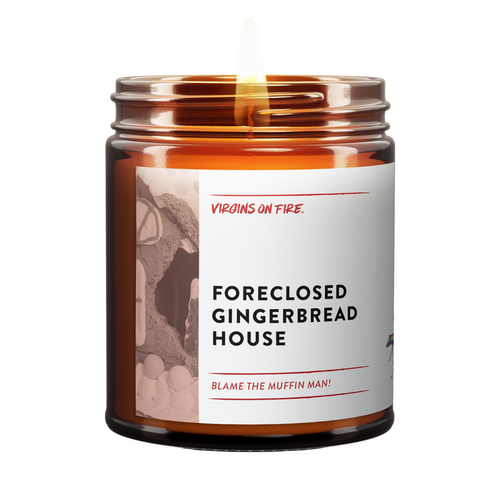 Amber glass candle from Virgins On Fire Candle Co., a gay-owned Brooklyn, NY business. This funny candle label reads 'Foreclosed Gingerbread House' with humorous subtitle 'Blame the Muffin Man!' Features architectural imagery and lit wick